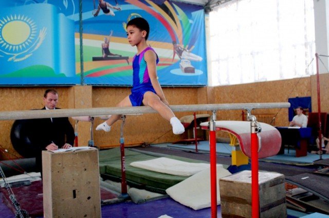 Юный гимнаст выполняет упражнение на параллельных брусьях